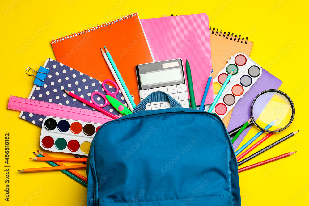 Backpack with different stationery on yellow background, closeup