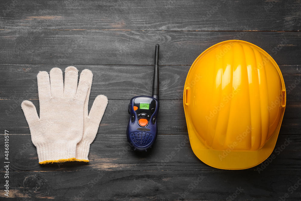 Safety hardhat with gloves and radio transmitter on dark wooden background