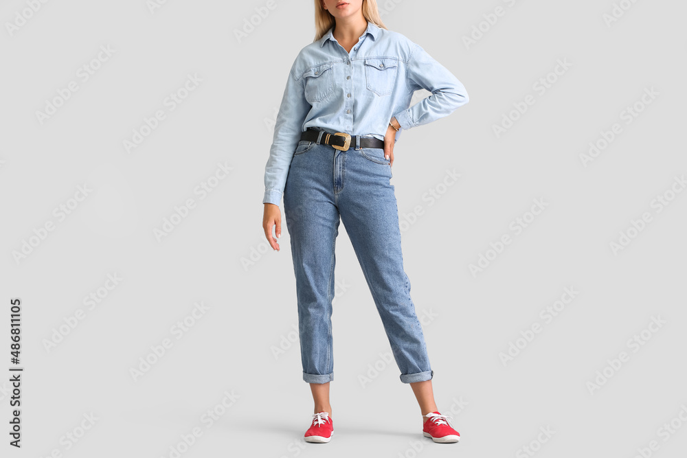 Fashionable young woman in stylish jeans clothes on light background