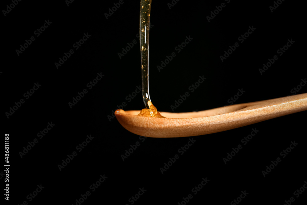 Honey dripping into wooden spoon on black background, closeup