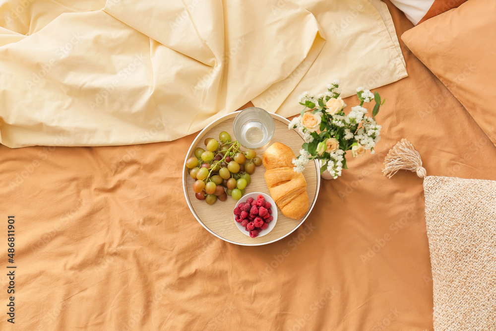 Tray with delicious breakfast and glass of water on comfortable bed