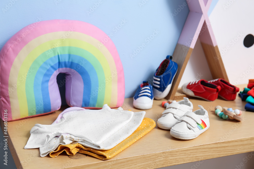 Bench with baby clothes and shoes near color wall