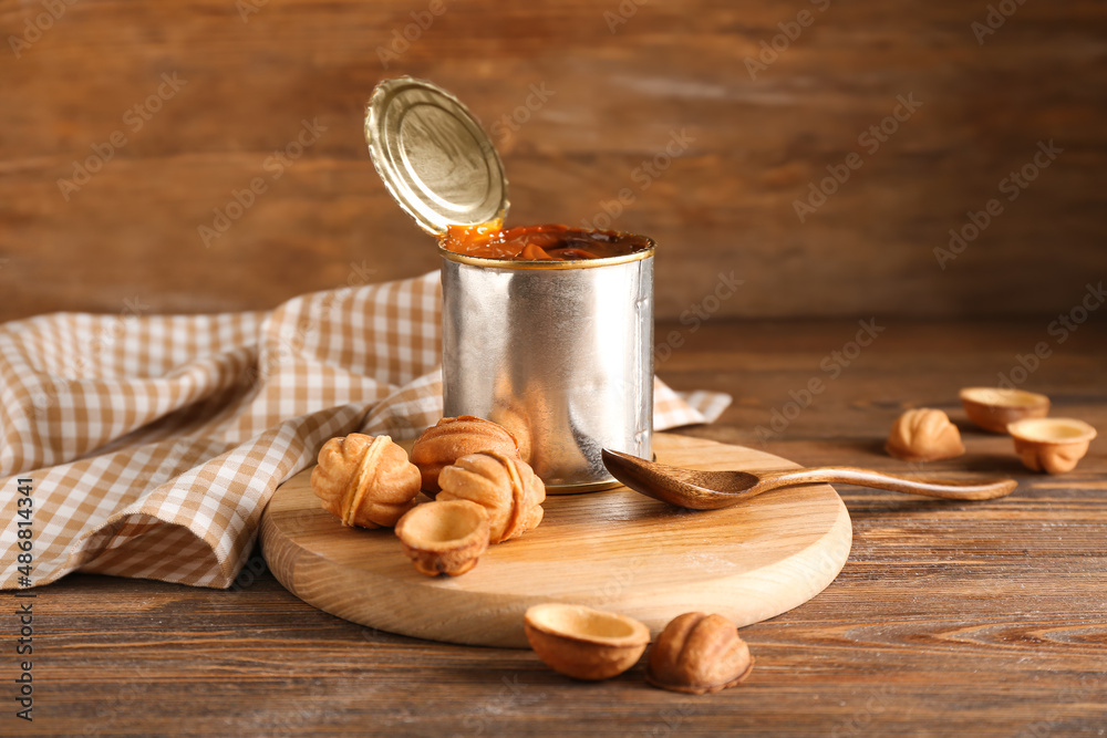 Tin can with boiled condensed milk and tasty walnut shaped cookies on wooden background