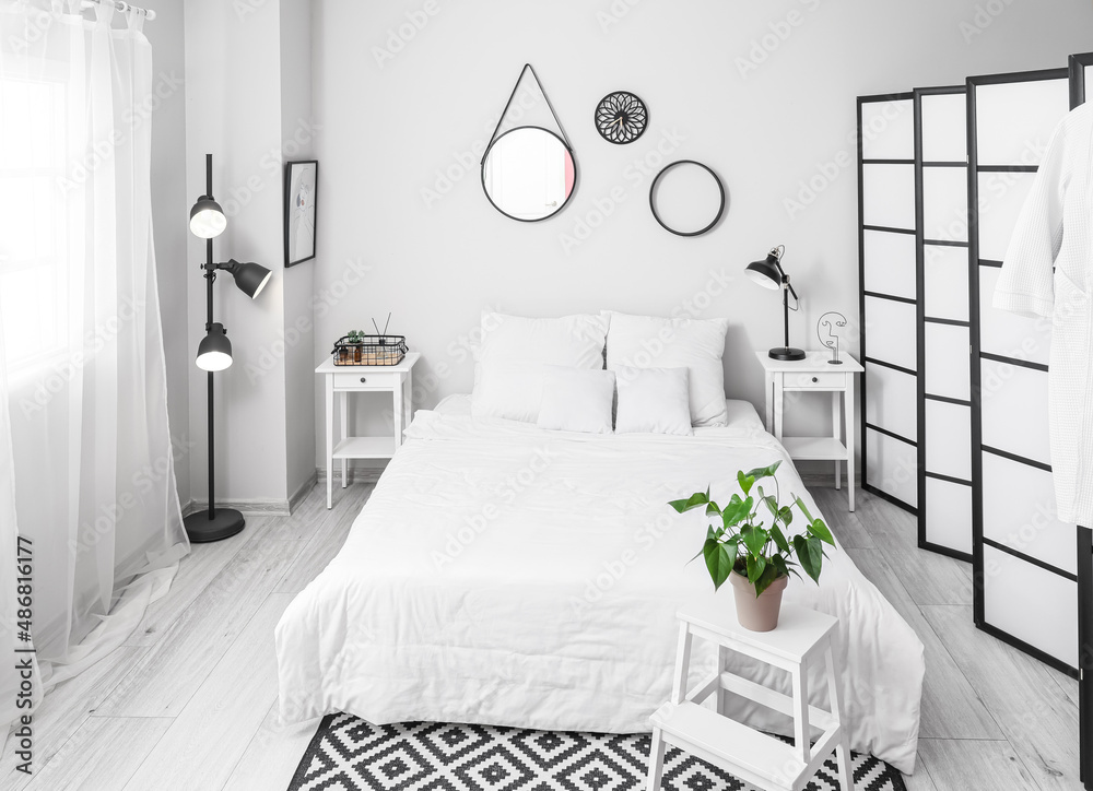 Interior of light bedroom with folding screen and glowing lamp