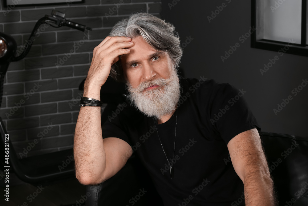 Portrait of handsome mature bearded man sitting in armchair at home