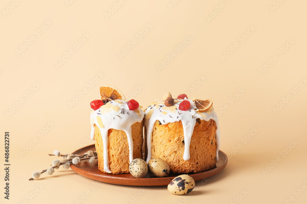 Plate with delicious Easter cakes, pussy willow branches and eggs on beige background