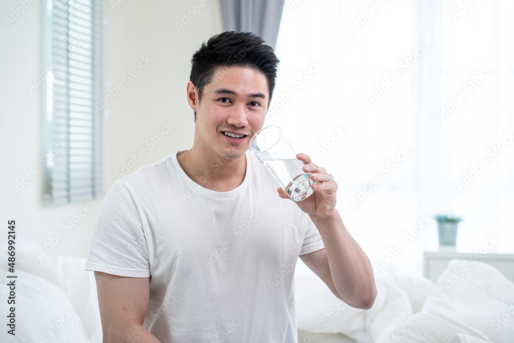 Portrait of Asian active strong man holding clean water in bedroom. 