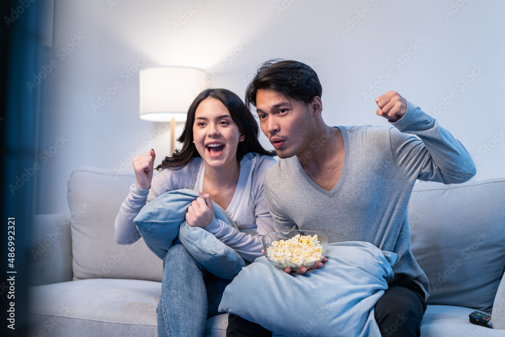 Asian new marriage couple watching football sport game on television. 