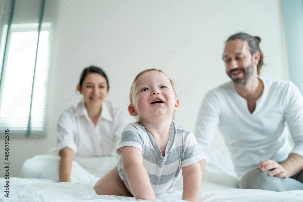 Caucasian parents playing with cute baby boy child on bed in bedroom. 