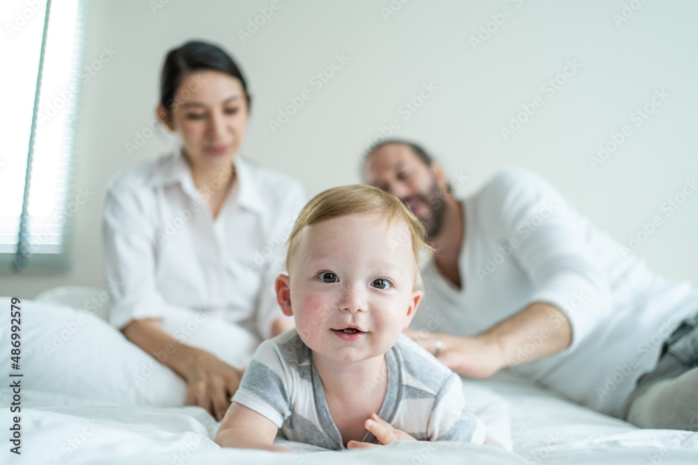 Caucasian parents playing with cute baby boy child on bed in bedroom. 