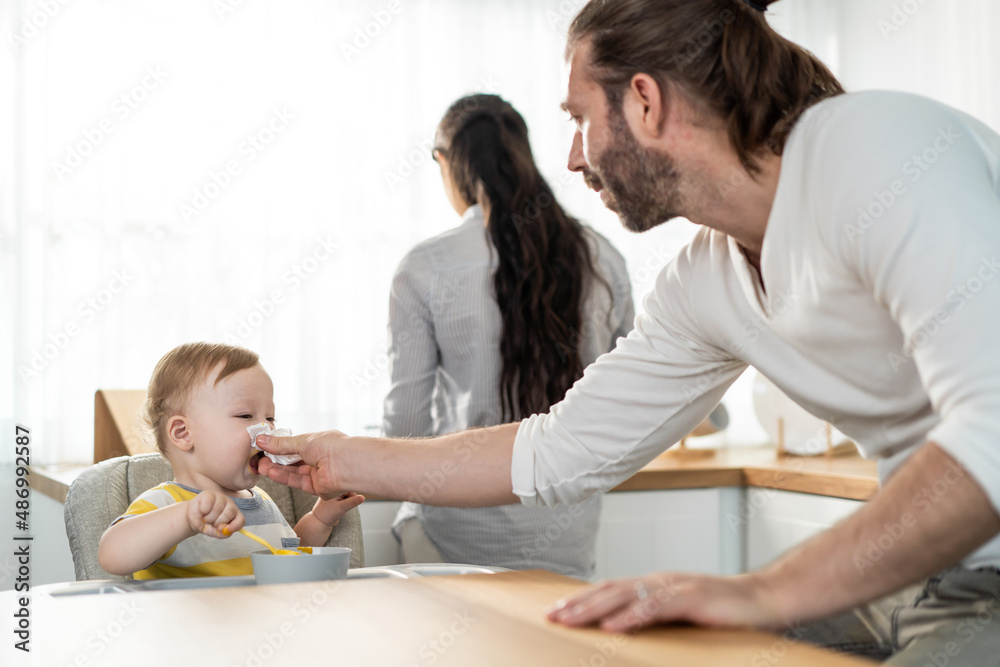 Caucasian beautiful parents take care of baby boy toddler in kitchen. 