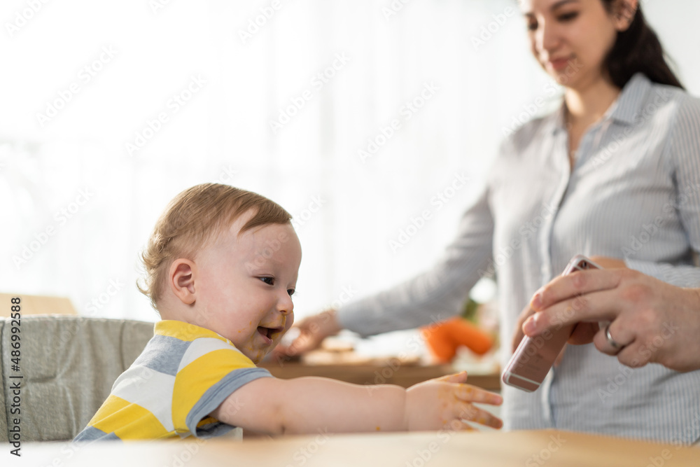 Young mother and baby boy video call online with family while eating. 