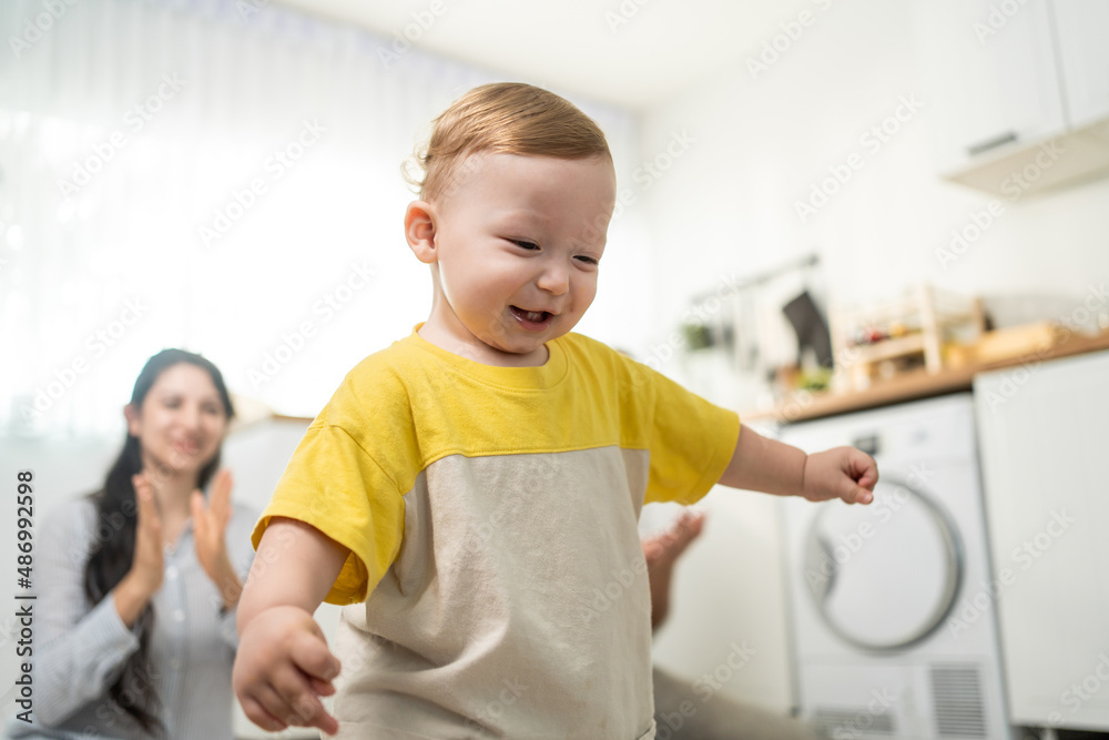 Caucasian baby boy child learn to walk with parents support in house. 