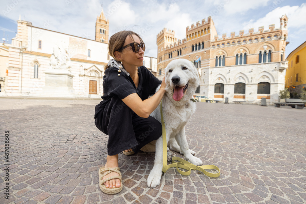 Woman with dog traveling in Grosseto town the center of Maremma region in Italy. Maremmano abruzzese