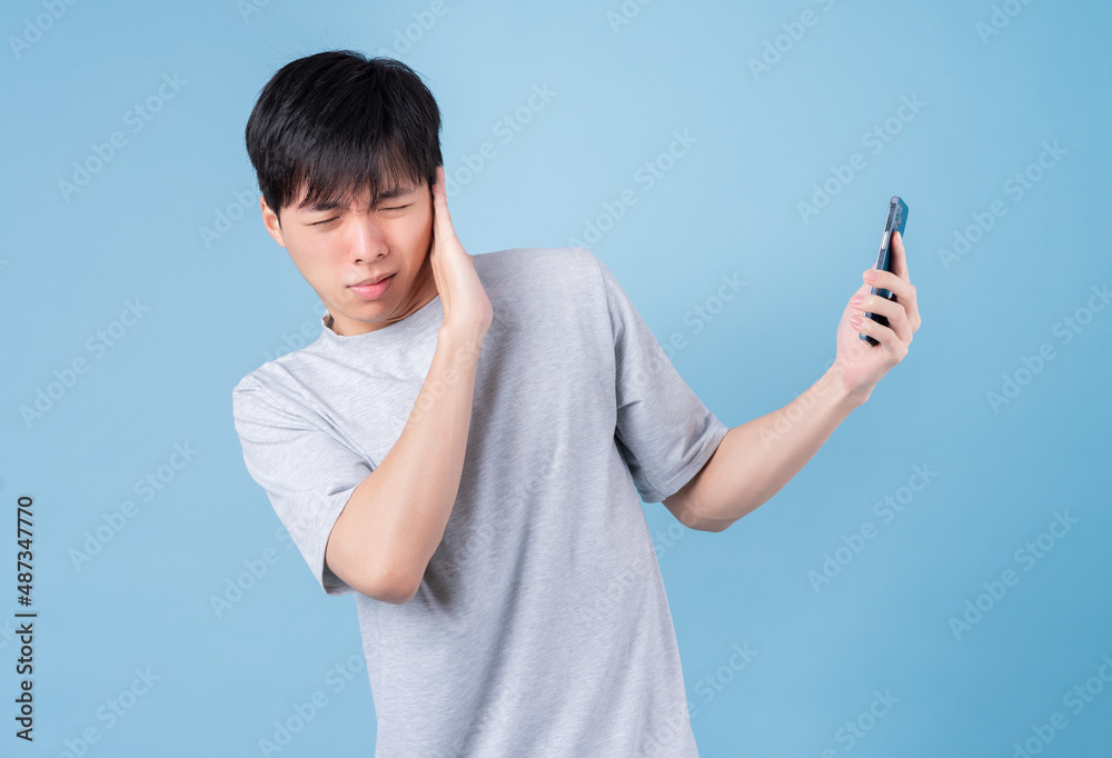 Young Asian man using smartphone on blue background