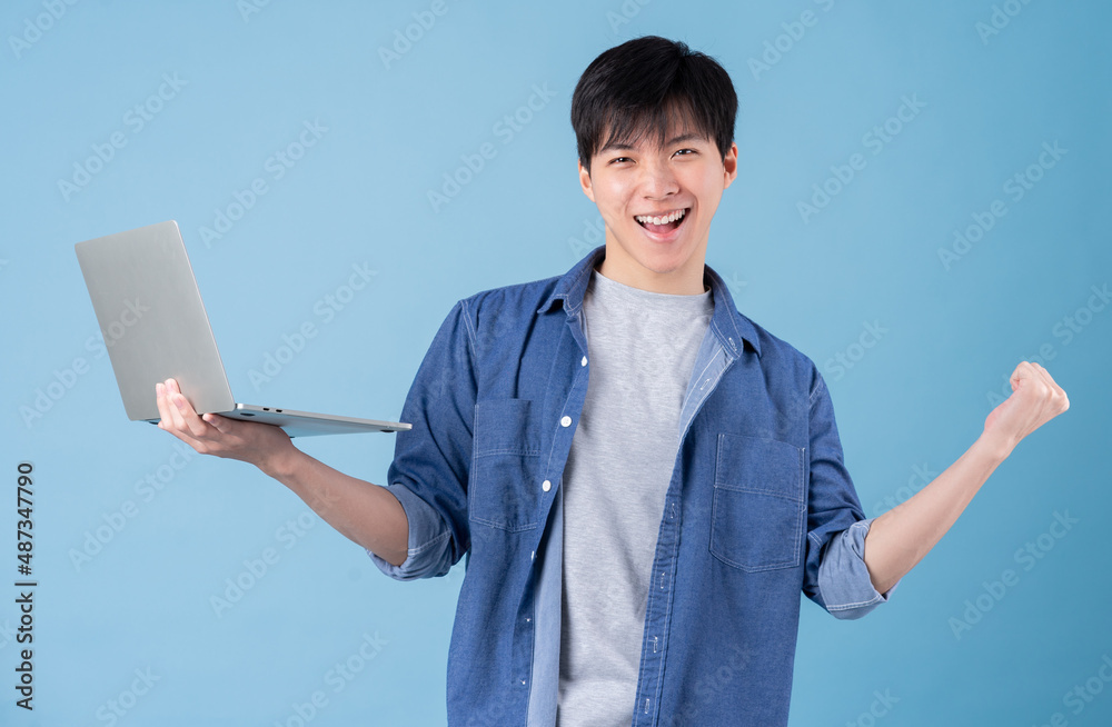 Young Asian man using laptop on blue background