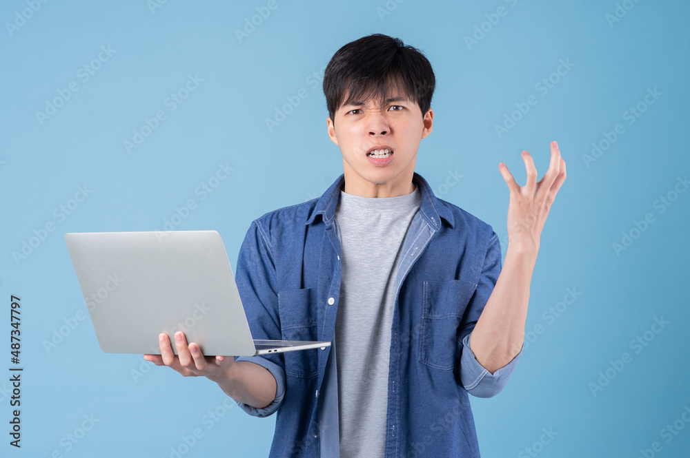 Young Asian man using laptop on blue background