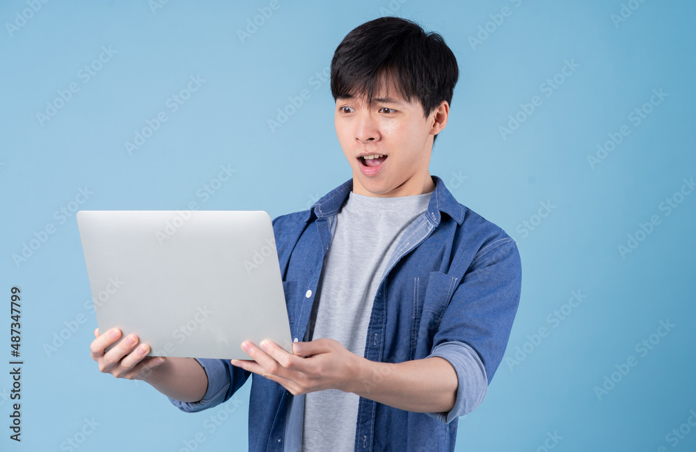 Young Asian man using laptop on blue background