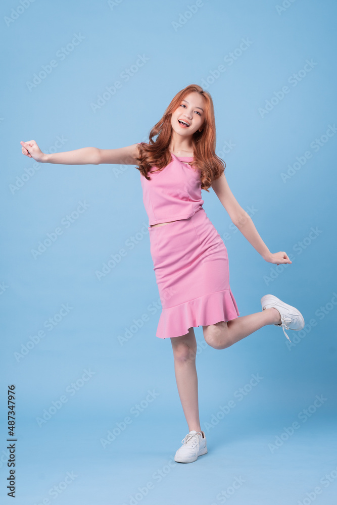 Young Asian woman wearing pink dress and posing on blue background