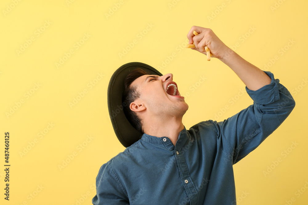 Emotional young man eating french fries on yellow background