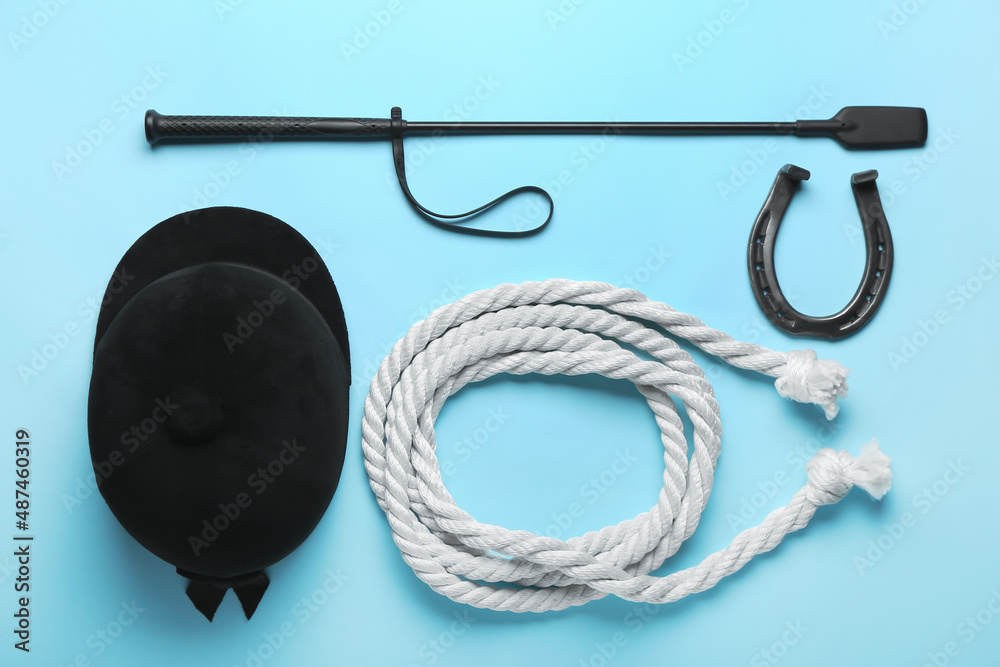 Horse riding helmet and crop with rope and horseshoe on color background