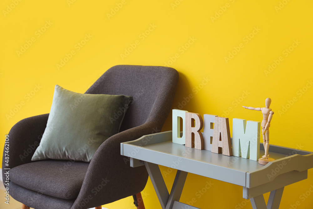 Coffee table with decor and soft armchair near yellow wall