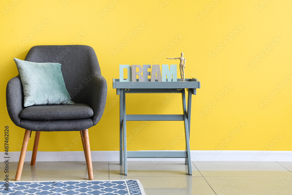 Coffee table with decor and soft armchair near yellow wall