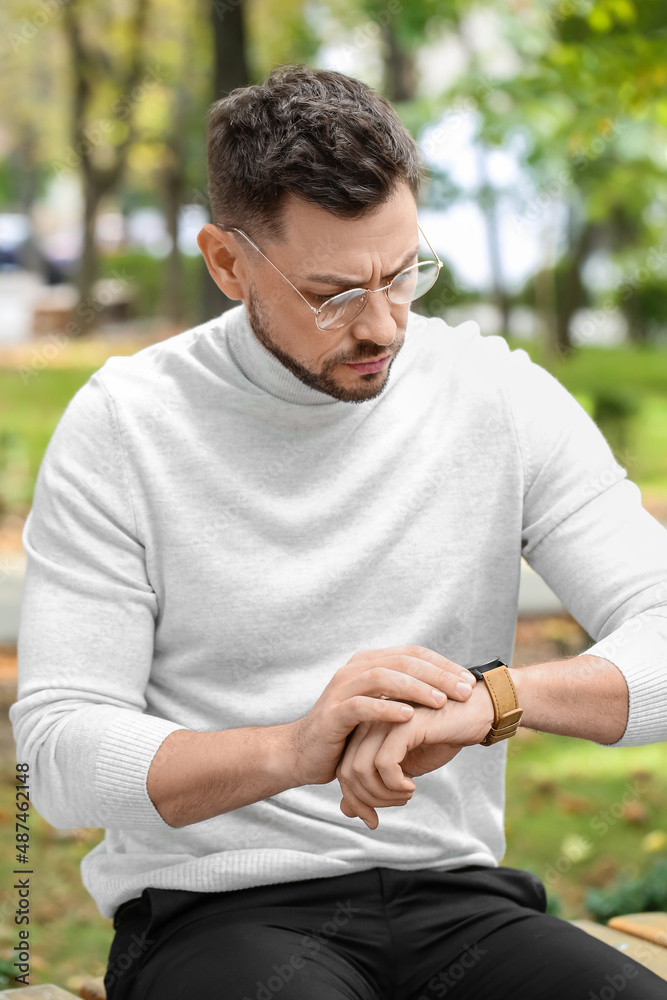 Stylish businessman looking at wristwatch in park