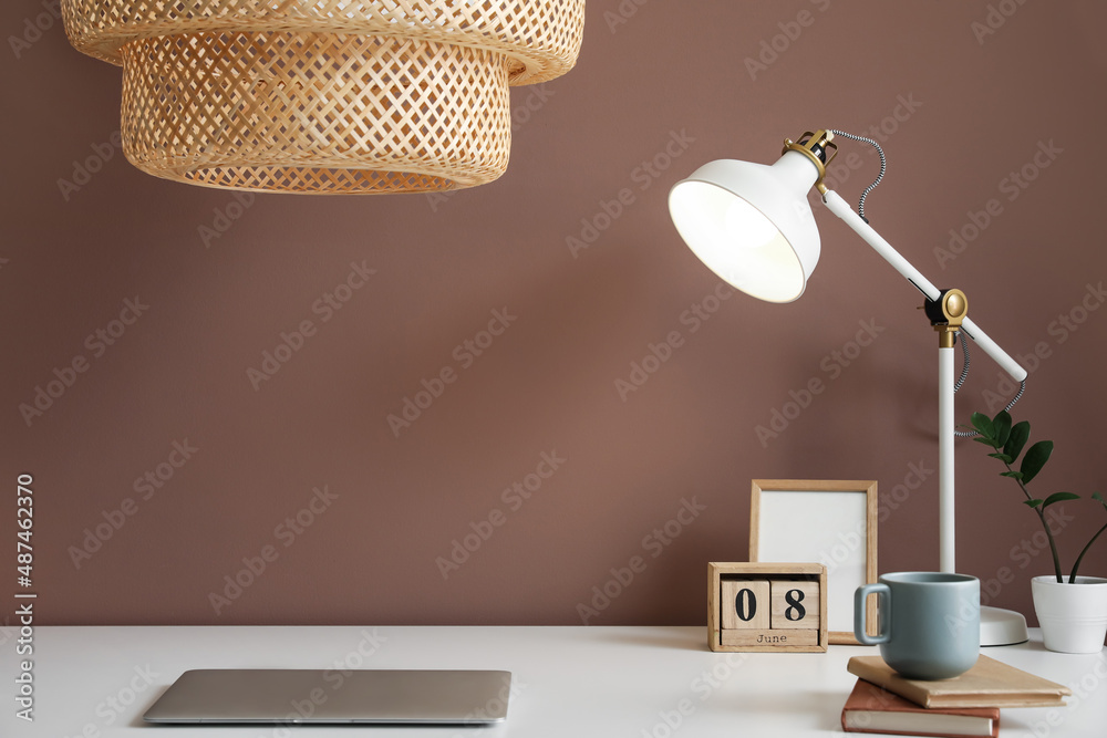 Modern workplace with laptop and lamps near brown wall