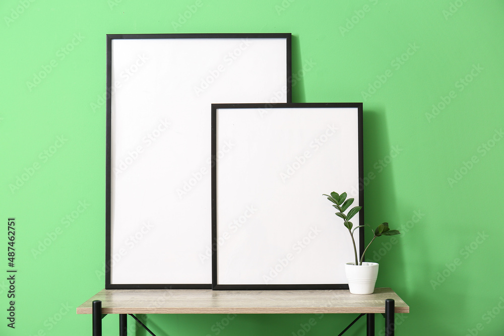 Blank frames and flowerpot on shelf near green wall