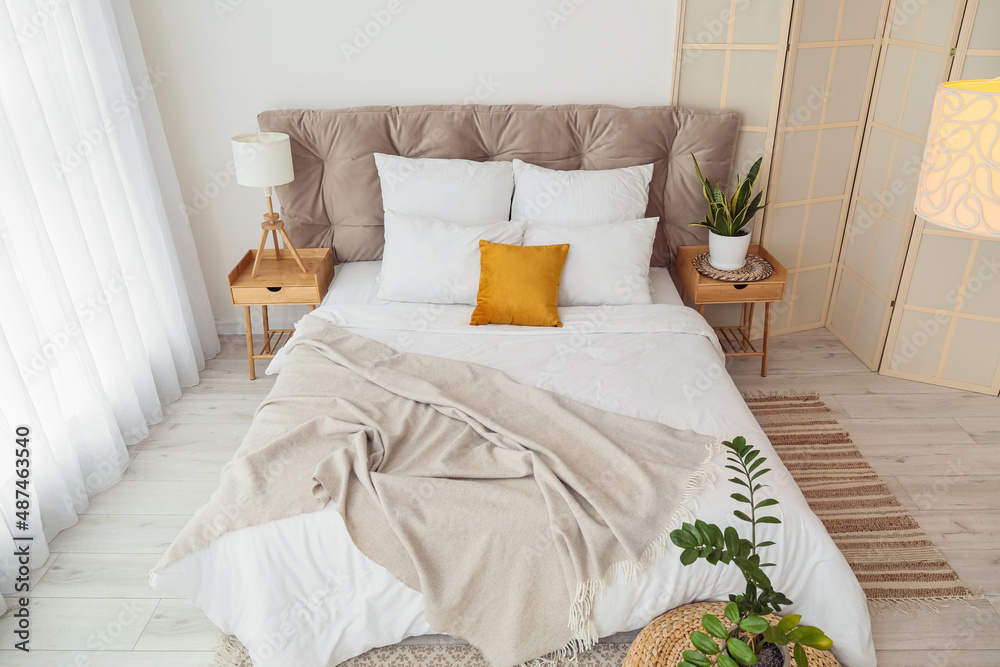 Interior of modern bedroom with stylish folding screen, nightstands and houseplants