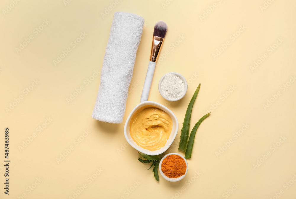 Bowls with turmeric mask, powder, makeup brush and aloe on beige background