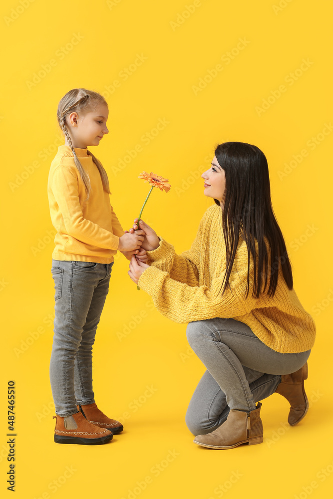 Little girl and her mother with flower on yellow background