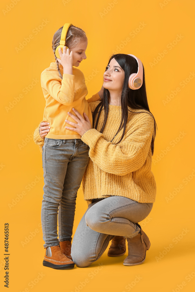 Little girl and her mother in headphones and warm sweaters on yellow background