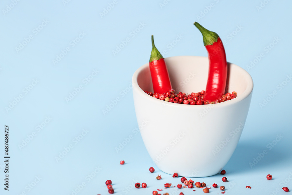 Bowl with chili peppers and red peppercorns on blue background