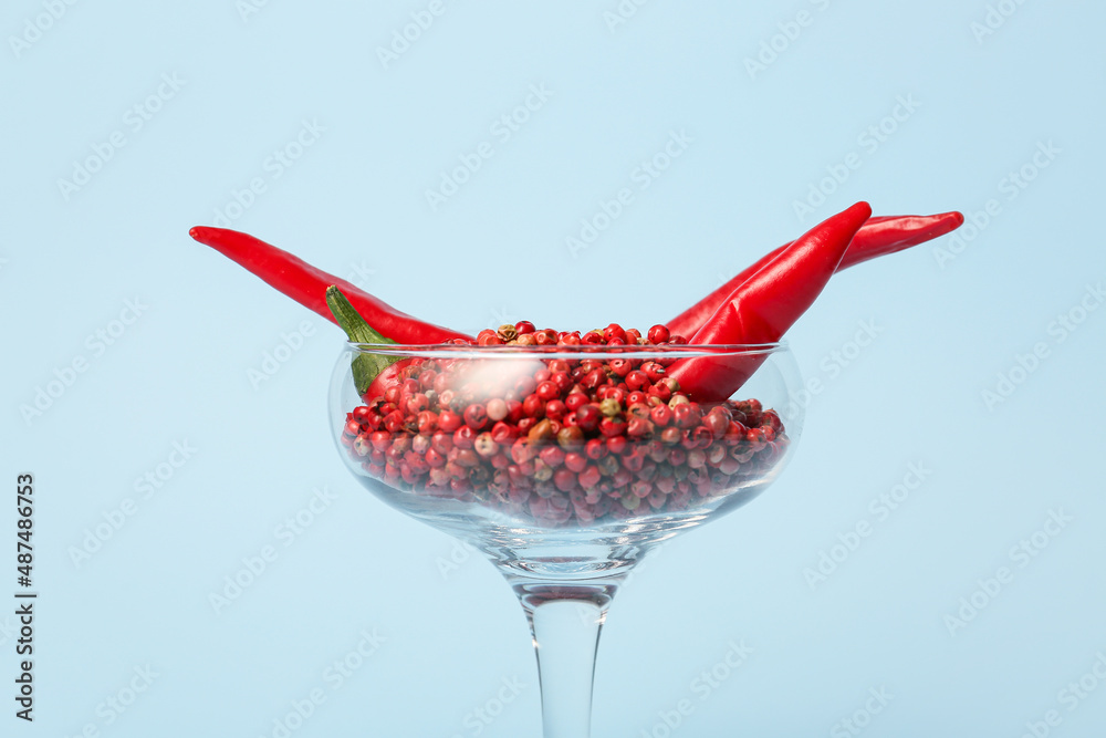 Glass with hot chili peppers and peppercorns on blue background