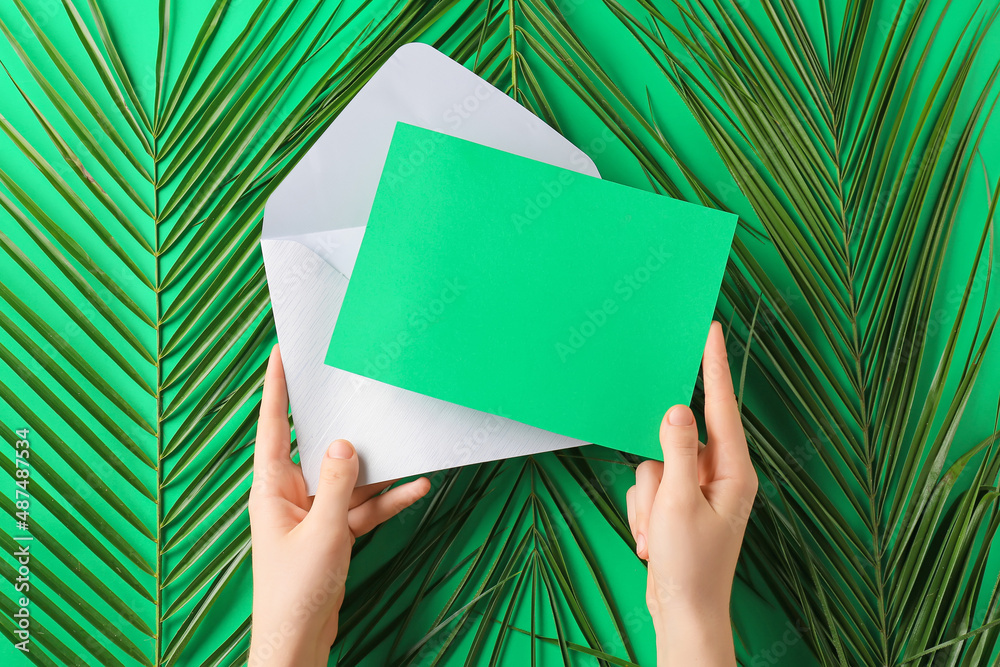 Female hands with blank card and palm leaves on green background