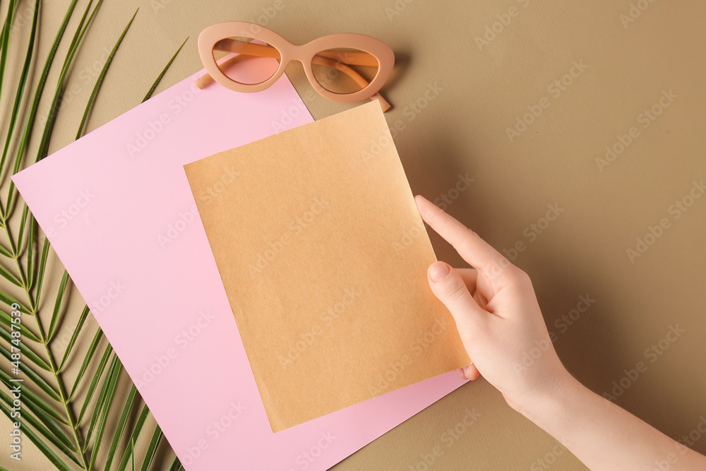 Female hand with blank cards, sunglasses and palm leaf on color background, closeup