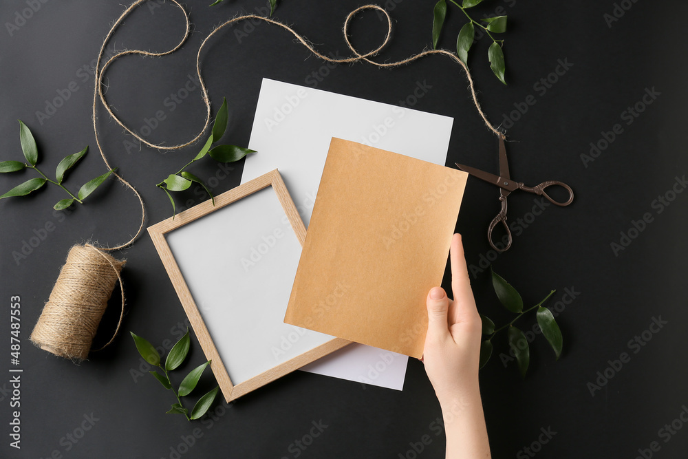 Female hand with blank card, picture, rope and scissors on dark background