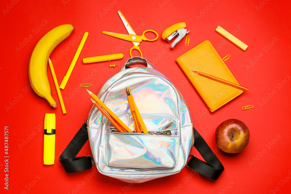 Stylish backpack, stationery, apple and banana on red background