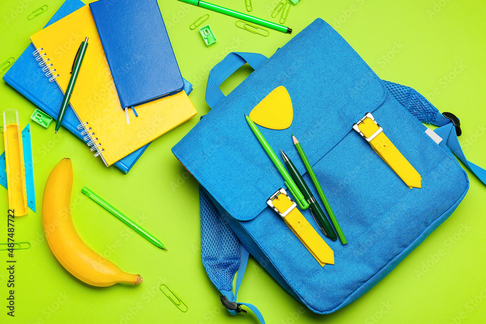 Backpack, stationery and banana on green background