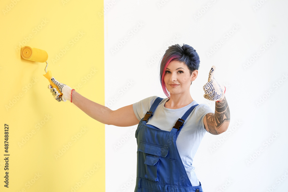 Female decorator painting yellow wall and showing thumb-up in room