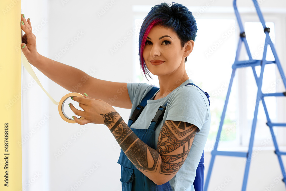 Female decorator with tape preparing wall for painting in room