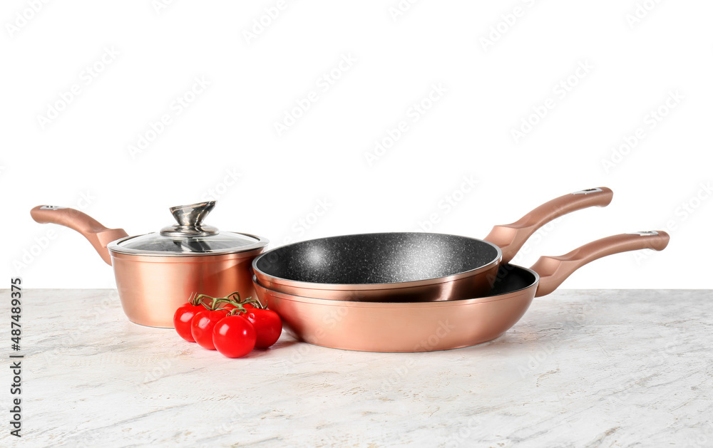 Copper saucepan with frying pans and tomatoes on table against white background