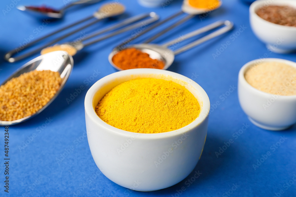 Bowl of turmeric powder on blue background, closeup