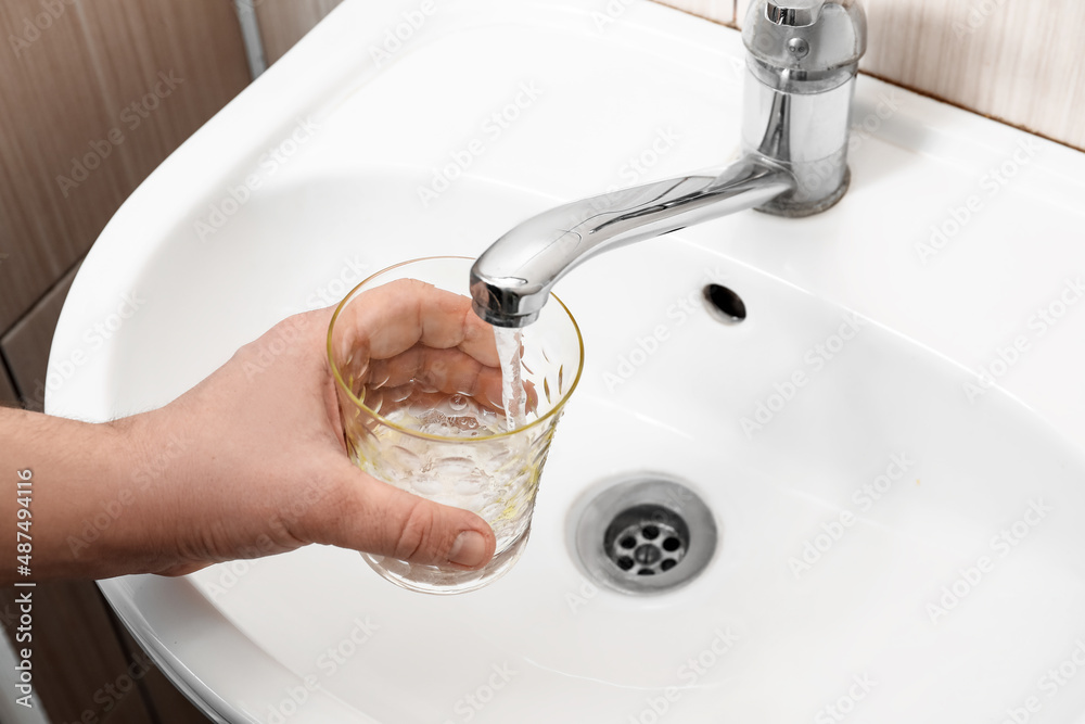 Man filling glass with water from tap in bathroom, closeup