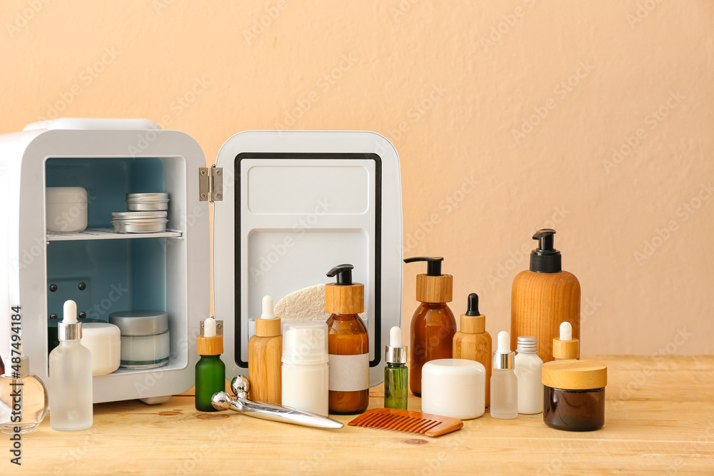 Small refrigerator with cosmetic products on wooden table