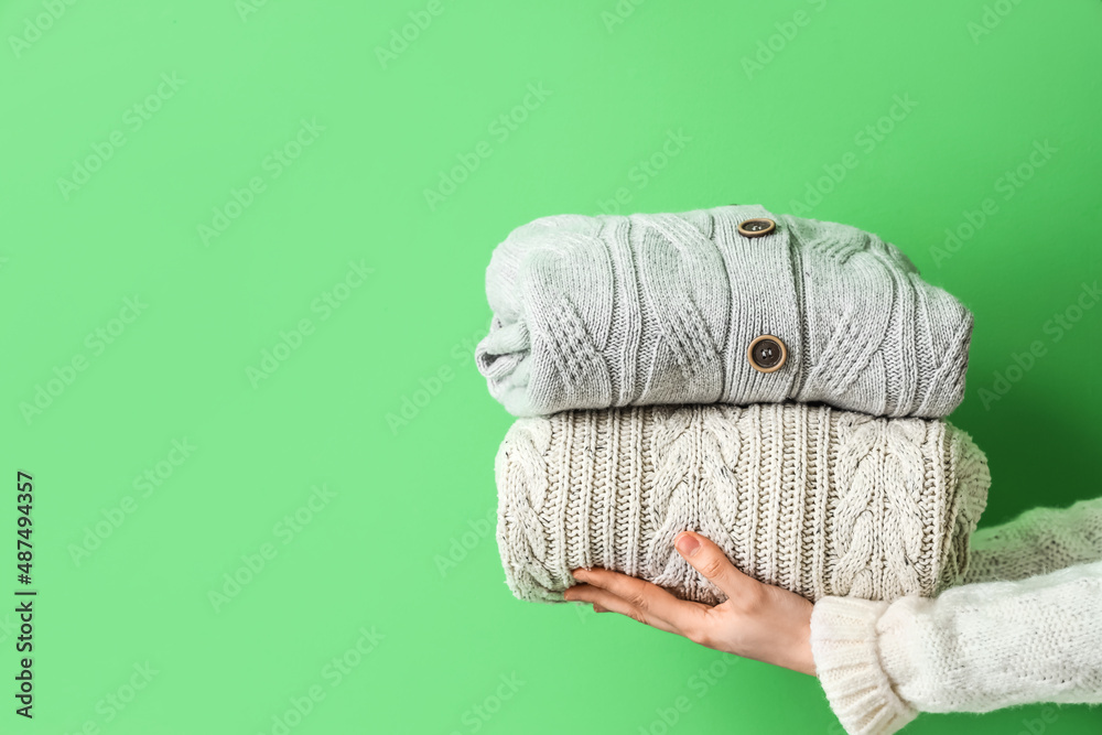 Woman holding stylish sweaters on color background