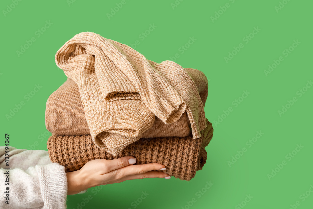 Woman holding warm sweaters on color background