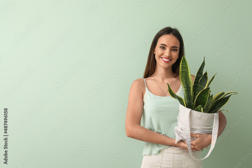 绿色背景下拿着室内植物环保袋的年轻女子